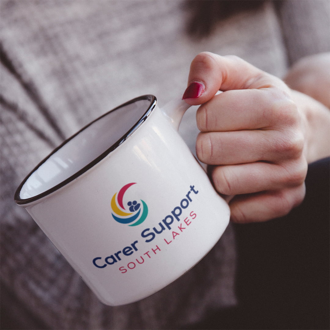Lady holding enamel mug which displays the Carer Support South Lakes logo