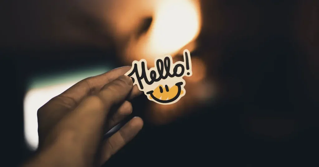 Hand holding a hello sticker on a darkened background