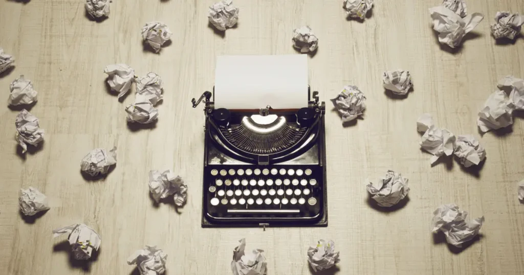 An old typewriter sat on a table amongst a collection of screwed up balls of paper